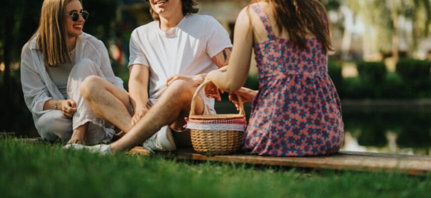 Three friends sitting on a blanket with a picnic basket in a grassy area